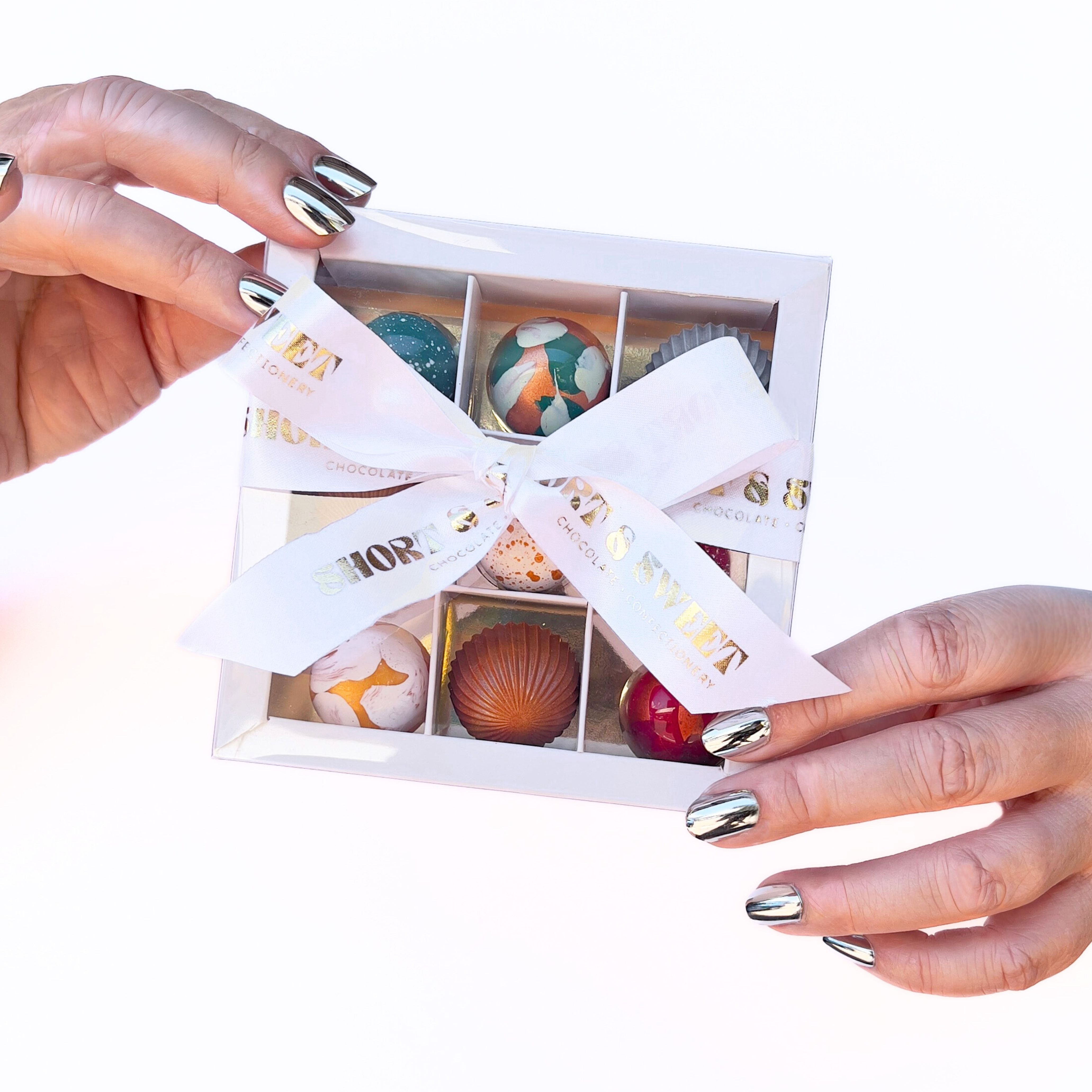 Hand holding a box of chocolates with a decorative ribbon on a white background