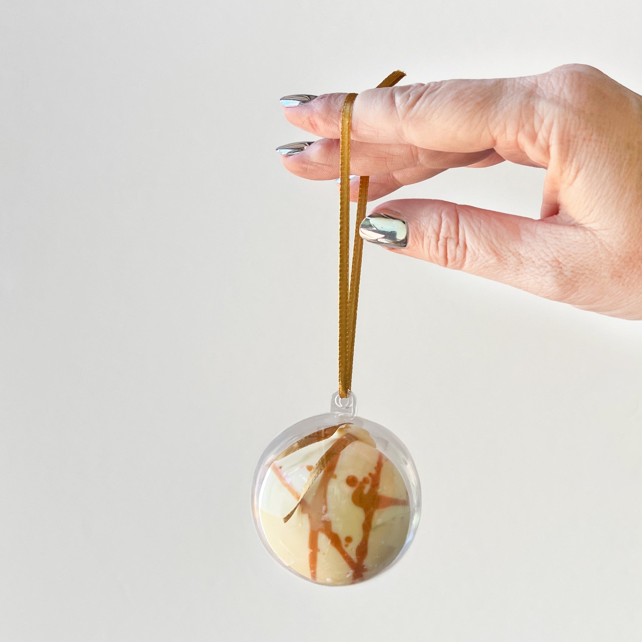 Hand holding a chocolate ornament with a ribbon against a white background