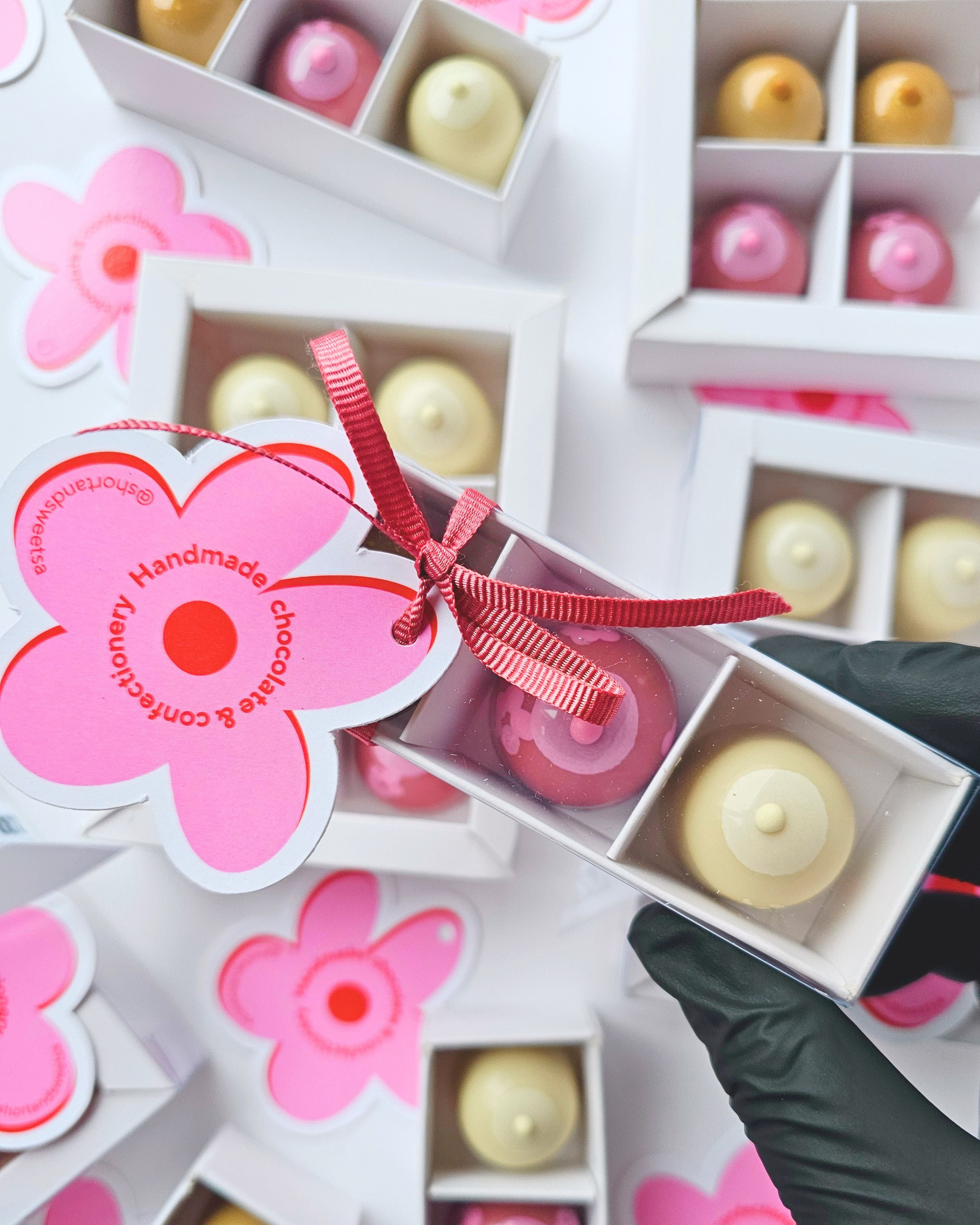 Handmade chocolate set with pink flower packaging and a hand holding one of the chocolates.
