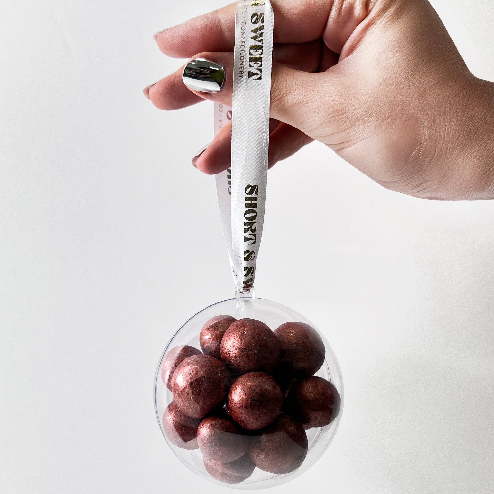 Hand holding a plastic bauble filled with chocolate coated cherries