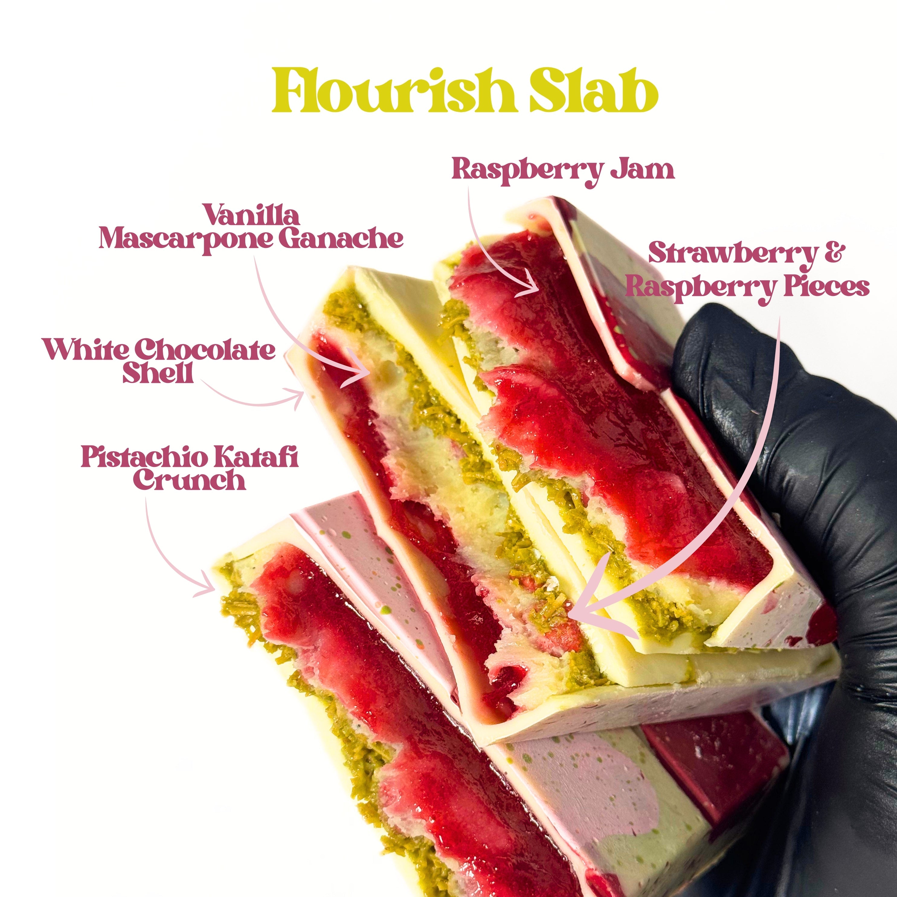 A hand wearing a black glove holds a layered dessert slab labeled with ingredients including raspberry jam, vanilla mascarpone ganache, white chocolate shell, strawberry and raspberry pieces, and pistachio katai crunch. The image has a white background with yellow 'Flourish Slab' text at the top.