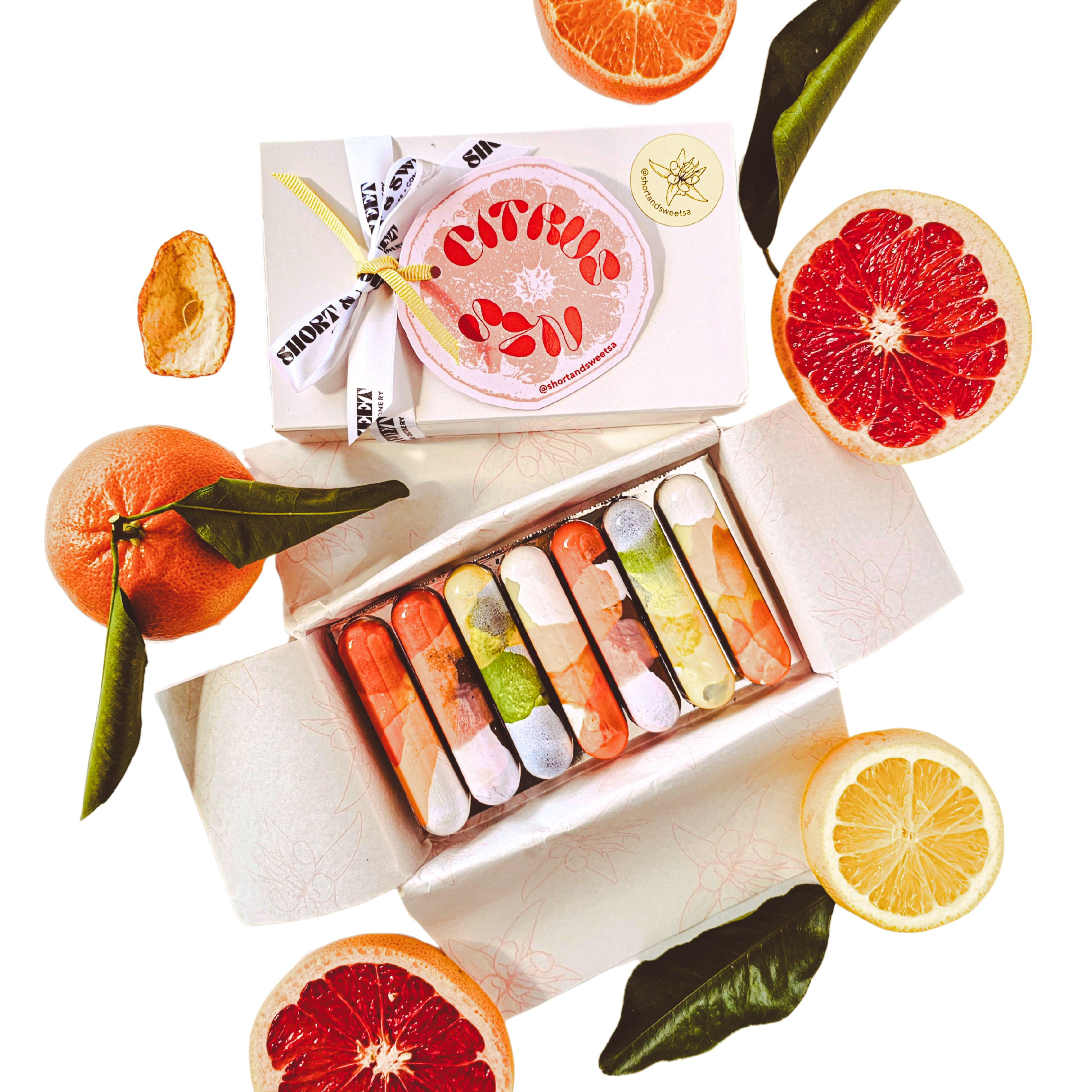 Box of colourful chocolate bars with sliced citrus fruits on a white background